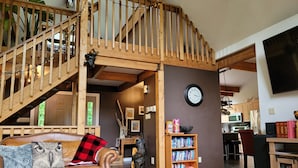 Ein gemütliches Wohnzimmer mit einer Holztreppe, einem Kamin, einem Bücherregal und einem Essbereich.