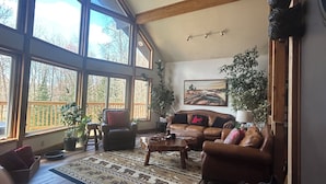 Ein geräumiges Wohnzimmer mit großen Fenstern, einem Ledersofa, einem Couchtisch und einem Bild an der Wand.