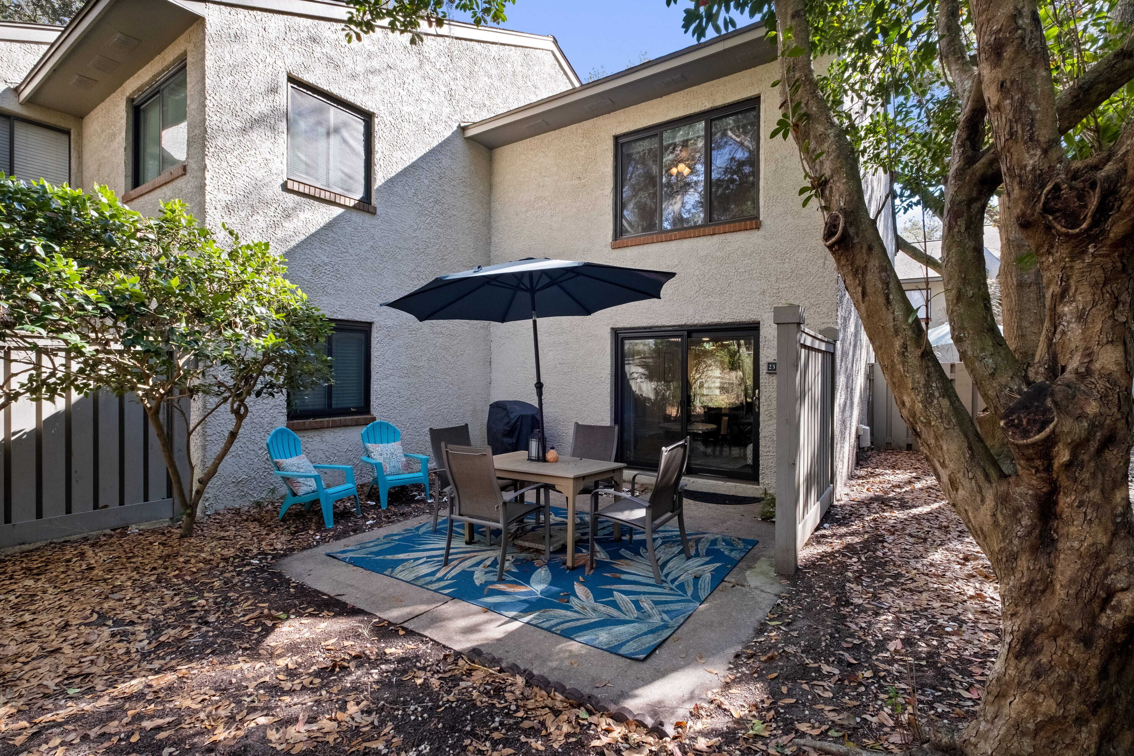 A patio with a table and chairs, an umbrella, and a tree.