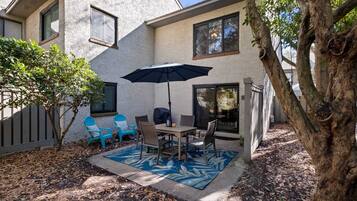 A patio with a table and chairs, an umbrella, and a tree.