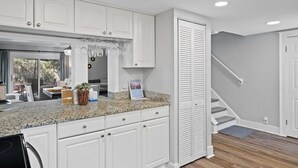 Cocina con armarios blancos, encimera de granito y una estantería colgante para vinos.