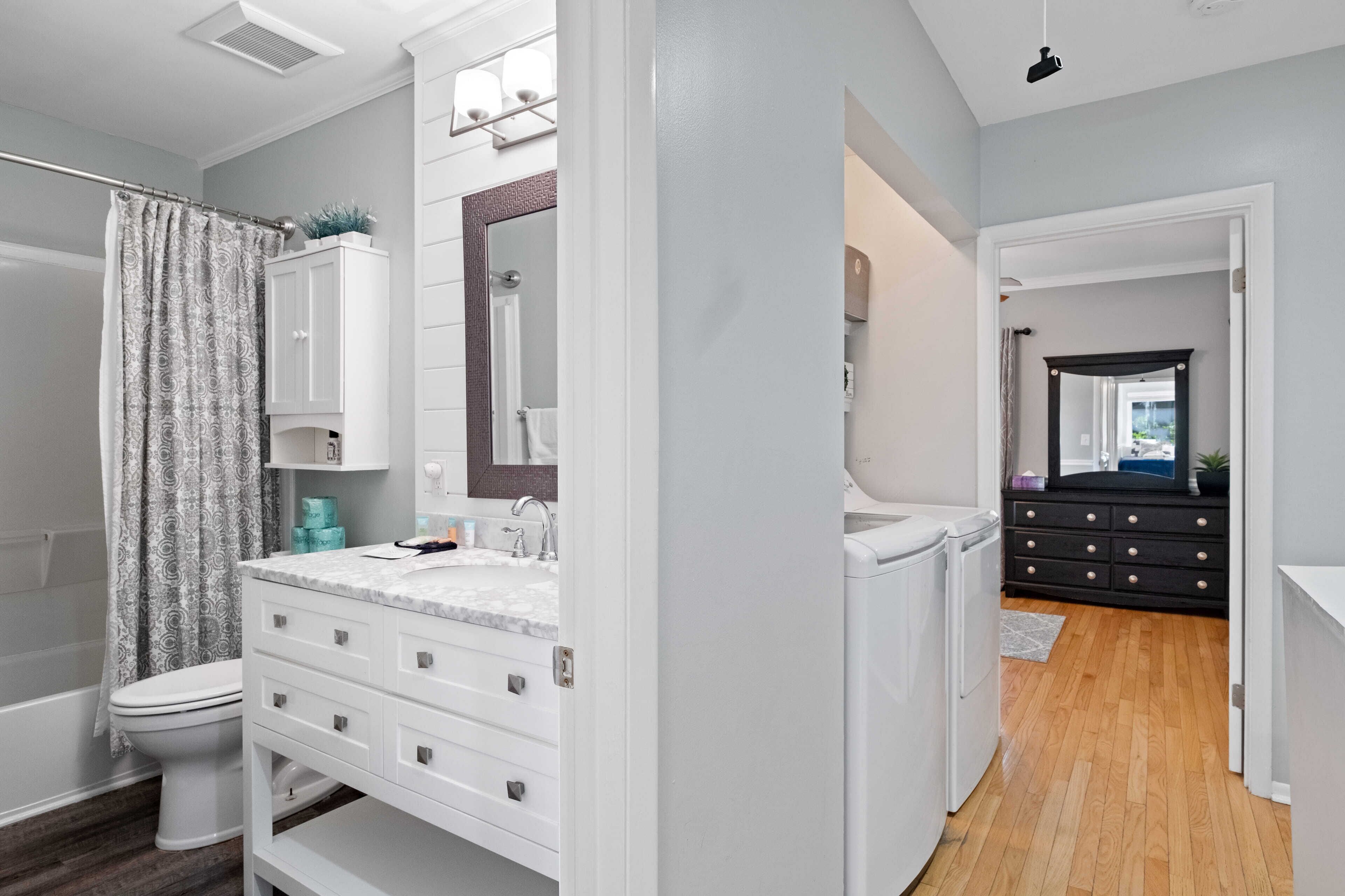 Une salle de bain moderne avec un meuble-lavabo blanc, un grand miroir, une douche et un plancher en bois.