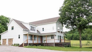 Uma casa branca de dois andares, com varanda coberta, garagem e acesso por um caminho de cascalho.