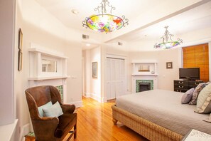A bedroom with a large bed, a chair, a television, and a fireplace.