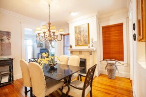 A dining room with a dark wooden table, beige upholstered chairs, a chandelier, and a fireplace with a mantel.