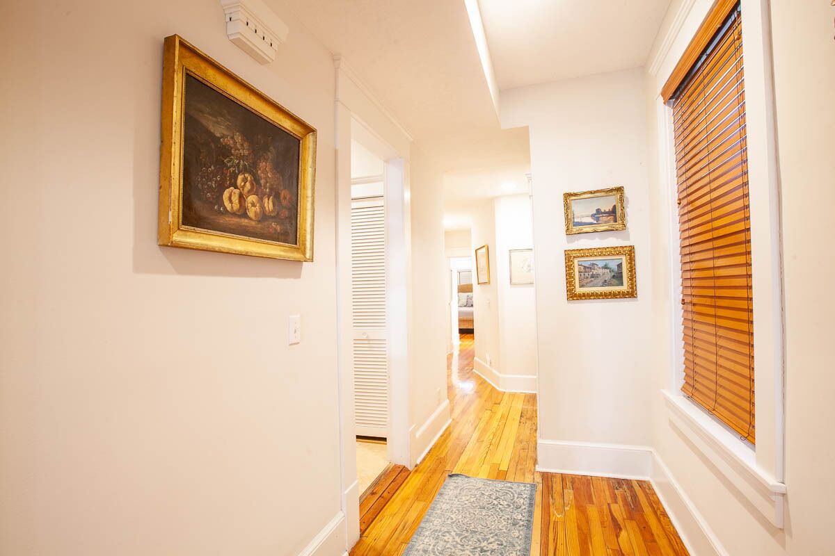 A hallway with wooden flooring, white walls, and framed artwork.