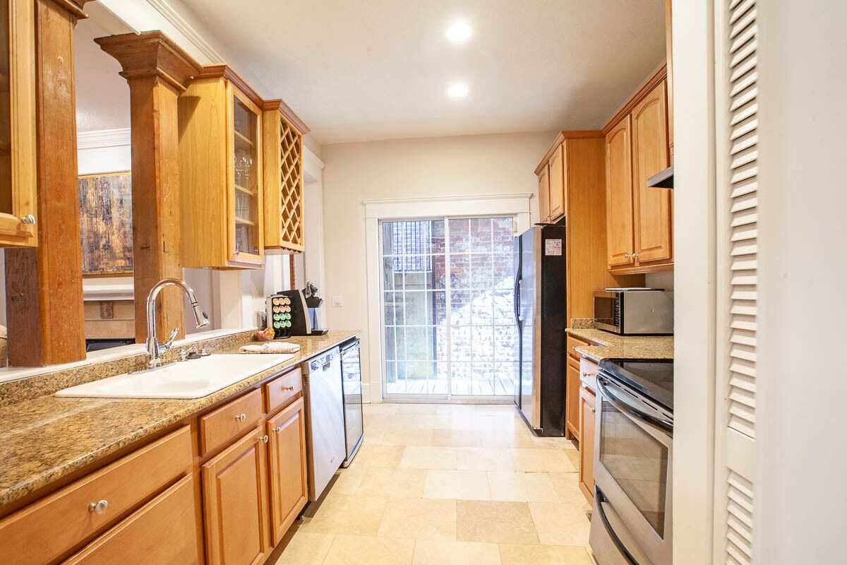 A kitchen with wooden cabinets, a granite countertop, a sink, a refrigerator, and an oven.