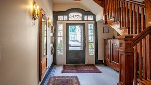 Un couloir avec un escalier en bois, une porte noire avec une fenêtre et un tapis sur le sol.