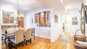 Un coin repas avec une table et des chaises en bois, un lustre, et un espace cuisine doté de meubles en bois et d’une fenêtre.