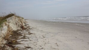 A sandy beach with a white wall and sparse vegetation. -  @ Ocean Front Guest Friendly Home "An Emerald On The Beach" (Sunset Beach)