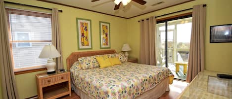 A bedroom with a bed, nightstand, lamp, ceiling fan, and large windows.
