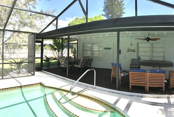 A swimming pool with a glass enclosure, a ceiling fan, and outdoor furniture.