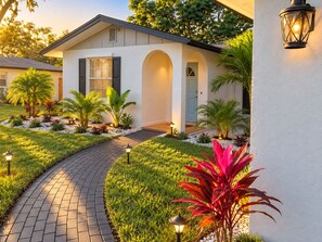 A modern house with a paved driveway, a well-maintained garden, and a door with a light fixture above it.