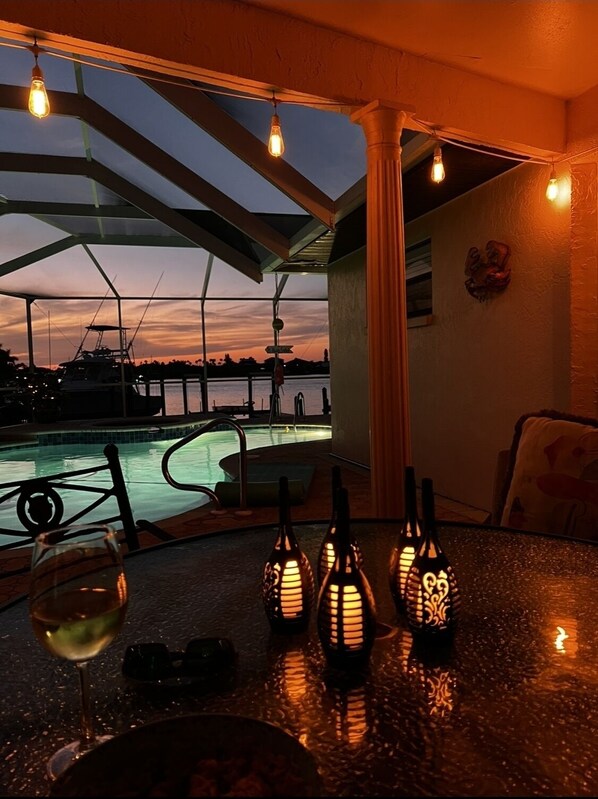 A poolside table with a glass of wine, three decorative lanterns, and a view of a marina at dusk. - Waterfront Pool Home with Dock directly On Bal Harbor (Apollo Beach)