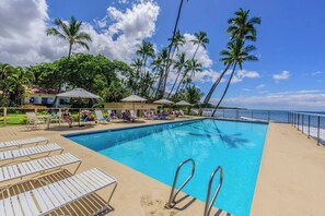 A pool area with lounge chairs, umbrellas, and palm trees.