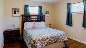 A bedroom with a wooden headboard, a bed with patterned bedding, a nightstand with a lamp, and two framed pictures on the wall.