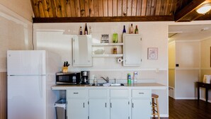 A compact kitchen with white cabinets, a microwave, a coffee maker, and a sink. There are bottles on the countertop and a sign above the sink. - Ash Creek Suite - In Downtown Historic Hermann (Hermann)