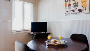 A dining area with a round table, chairs, a tray with food and drinks, a television, and a poster on the wall. - Ash Creek Suite - In Downtown Historic Hermann (Hermann)