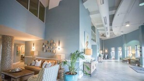 Un vestíbulo amplio con techo alto, una zona de estar con sofá y sillones, una planta grande en maceta y un mostrador de recepción.