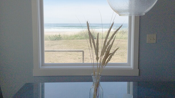 Une fenêtre donnant sur la plage, un vase contenant des plantes séchées et un luminaire suspendu.