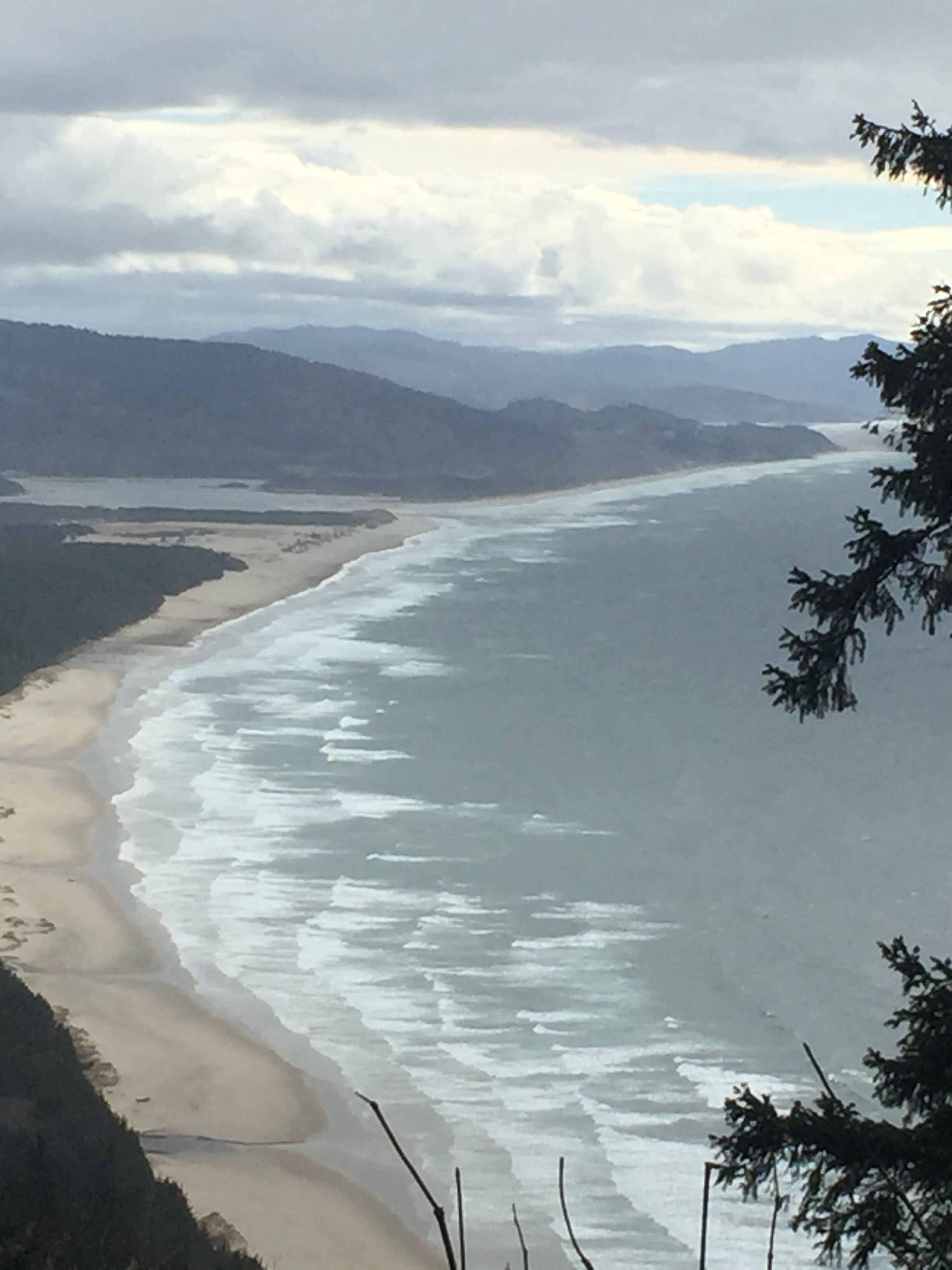 Un paysage côtier avec une plage, des vagues et des montagnes à l’horizon.