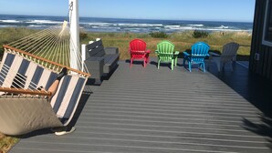 Une terrasse dotée d’un hamac, d’un banc et de quatre chaises Adirondack aux couleurs vives, toutes orientées vers l’océan.