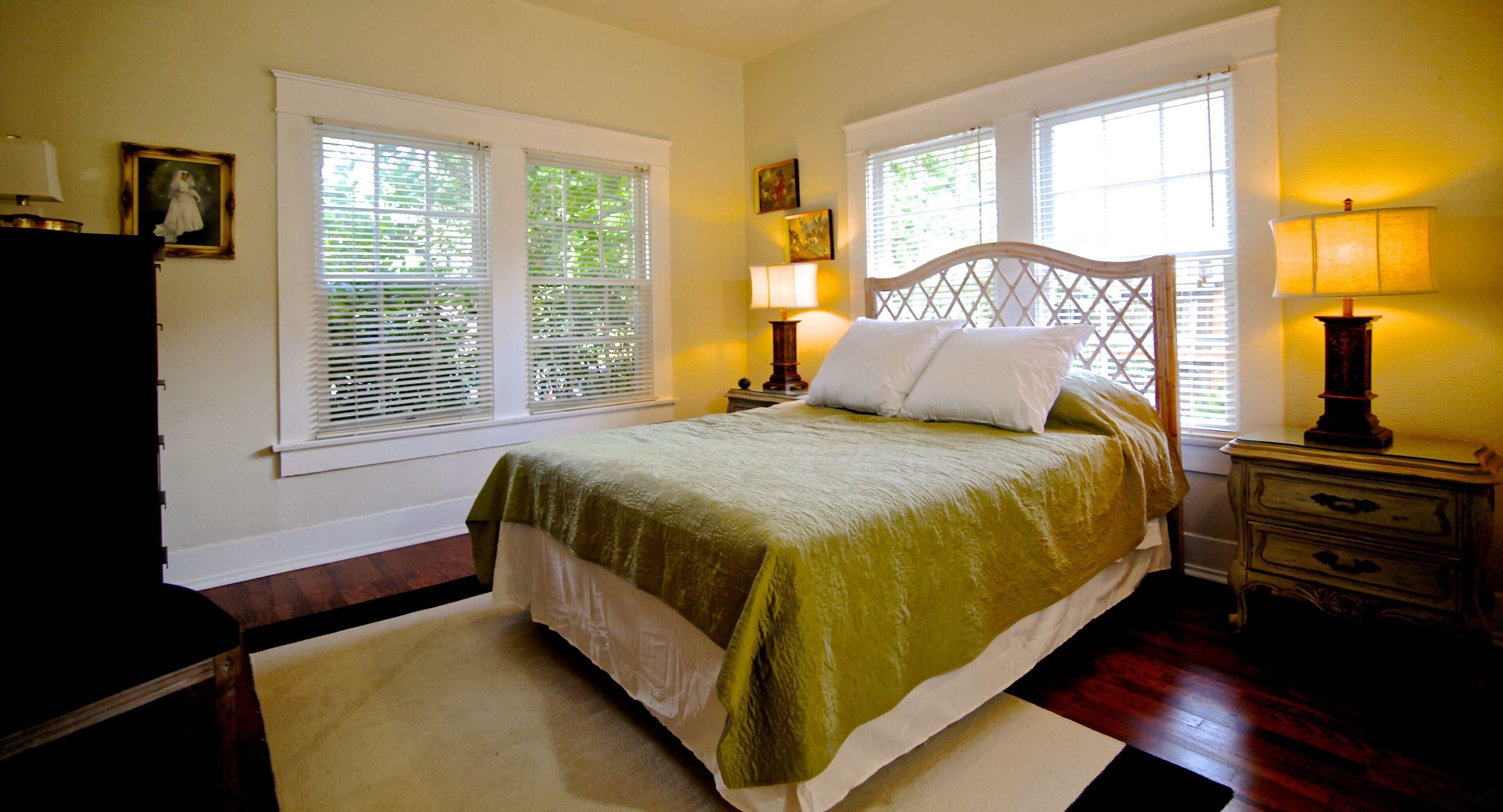 A bedroom with a bed, two bedside tables, a dresser, and a window with blinds.