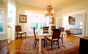 A dining area with a glass table and chairs, a chandelier, and a red patterned rug.