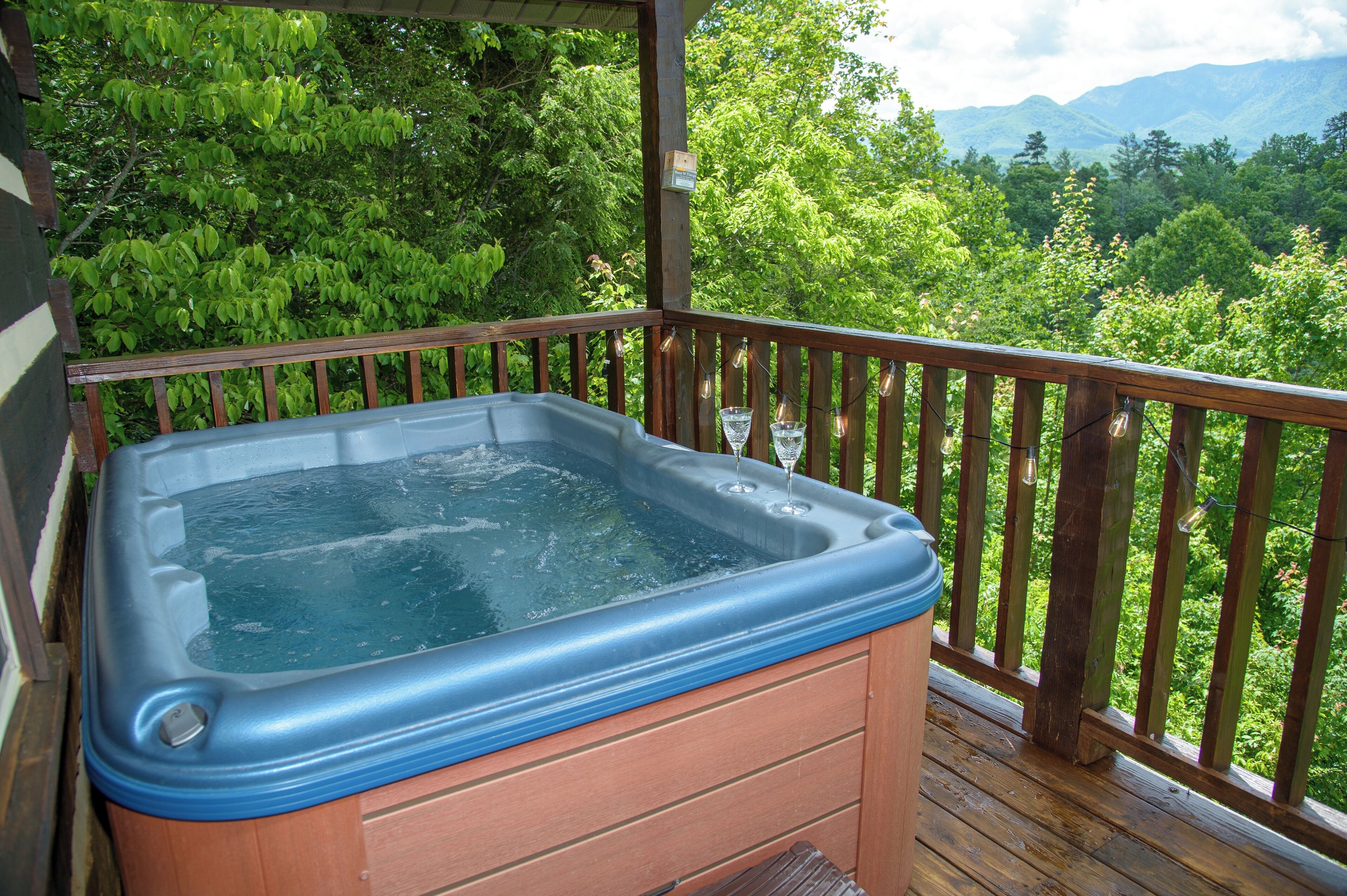 A hot tub on a wooden deck with a view of lush greenery and mountains in the background.