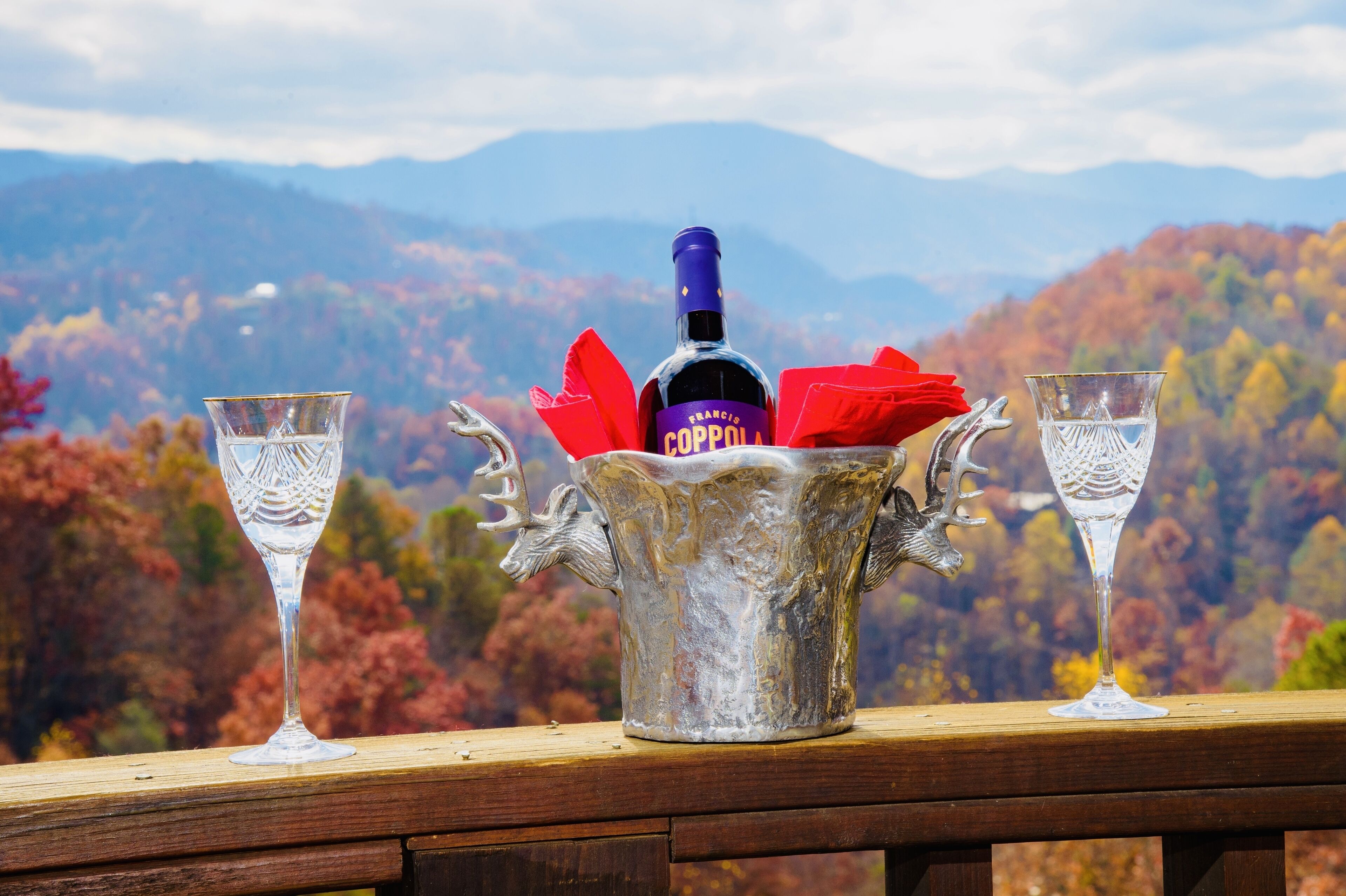 Una vista pintoresca con una botella de vino Francis Coppola y dos copas sobre una terraza de madera.