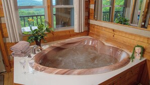 Casa de banho de cabana de madeira com uma banheira grande, janela com vista para vegetação e uma pequena planta no balcão.