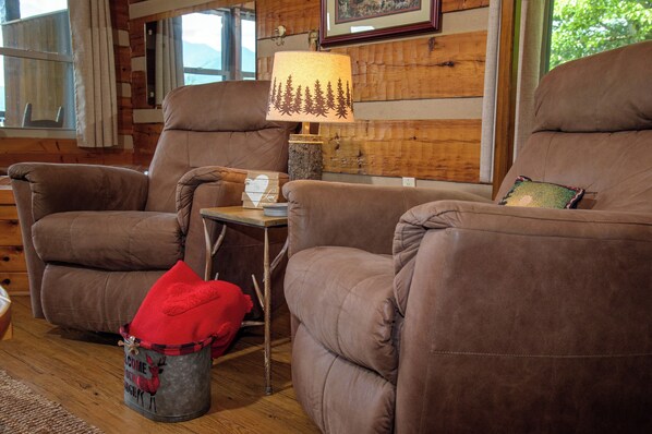 A cozy living room with two brown leather armchairs, a small wooden table with a lamp, and a decorative bucket with a reindeer design.