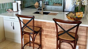 A modern kitchen with white cabinets, a stainless steel refrigerator, a coffee maker, and two wooden bar stools.