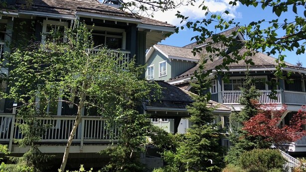 A two-story house with a front porch, surrounded by greenery and a clear blue sky.