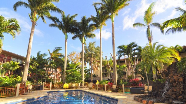 A swimming pool surrounded by palm trees and a stone wall with a waterfall. - Prince Kuhio Poipu ~ Ocean View, quiet, comfortable, end unit-ground floor (Koloa)