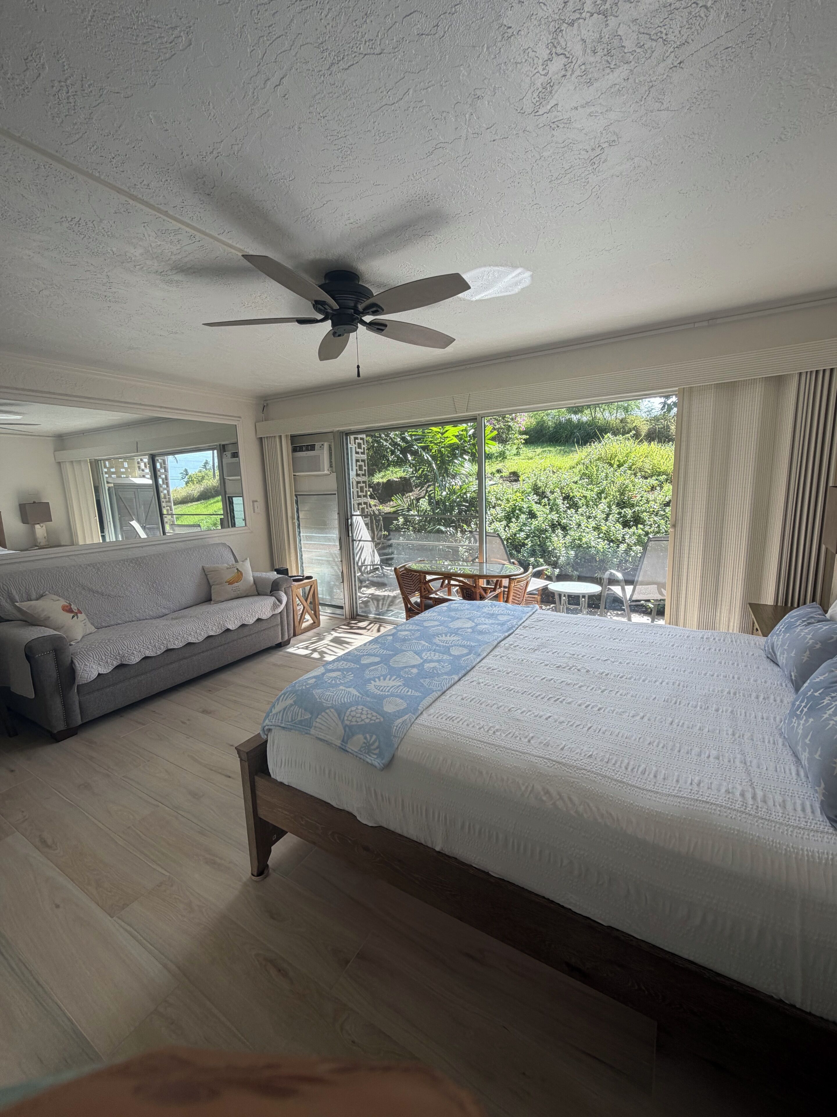 A bedroom with a large bed, a ceiling fan, a sofa, and a view of the outdoors.