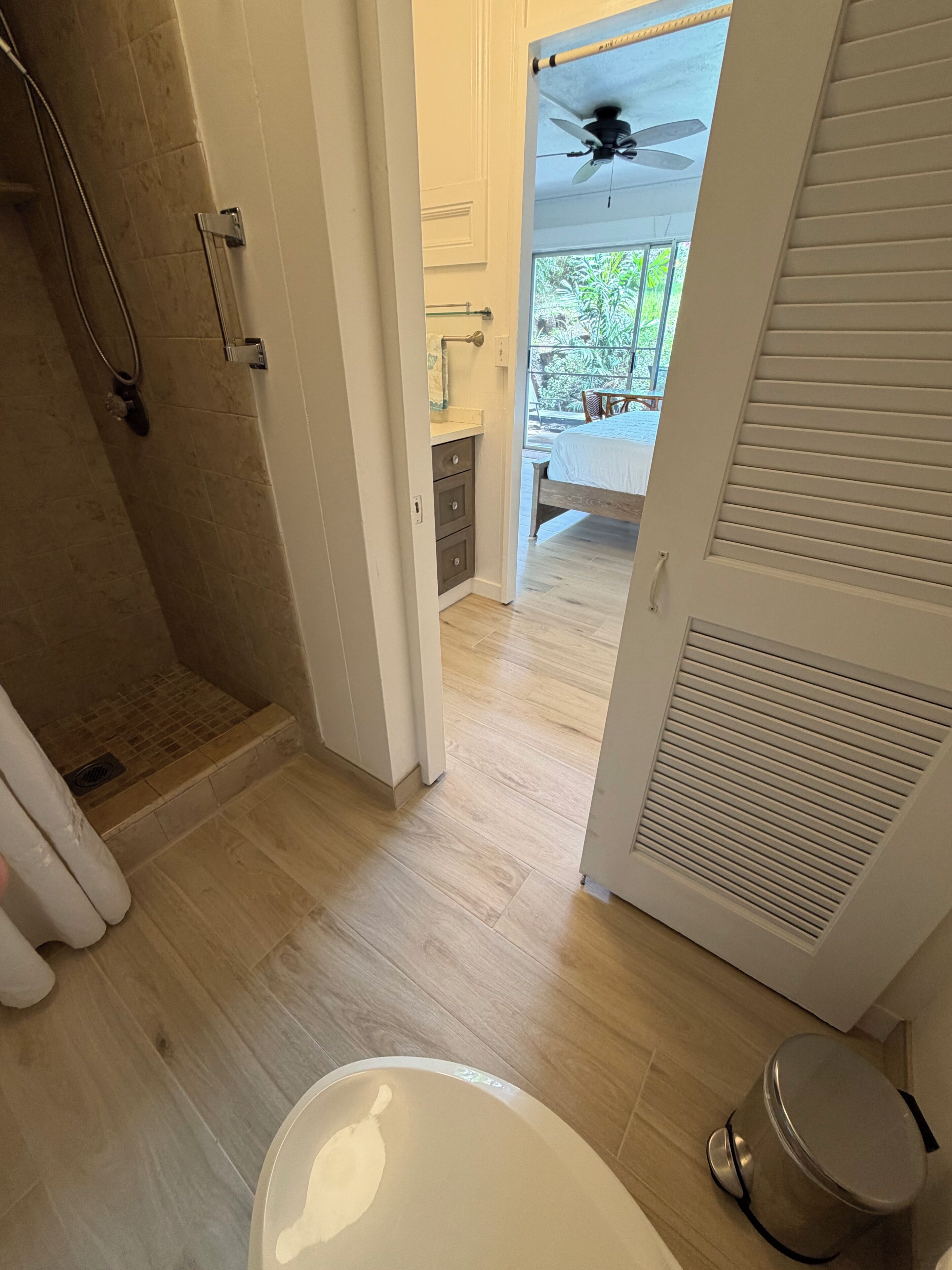 A bathroom with a shower, toilet, and a door leading to a balcony with a ceiling fan.