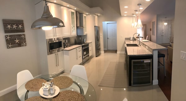 A modern kitchen with white cabinets, stainless steel appliances, and a glass dining table with woven placemats.