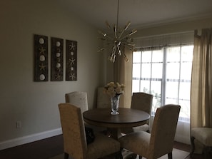 A dining area with a round table, four chairs, a vase with flowers, and wall art. - Luxury Golf Course Villa (Hudson)