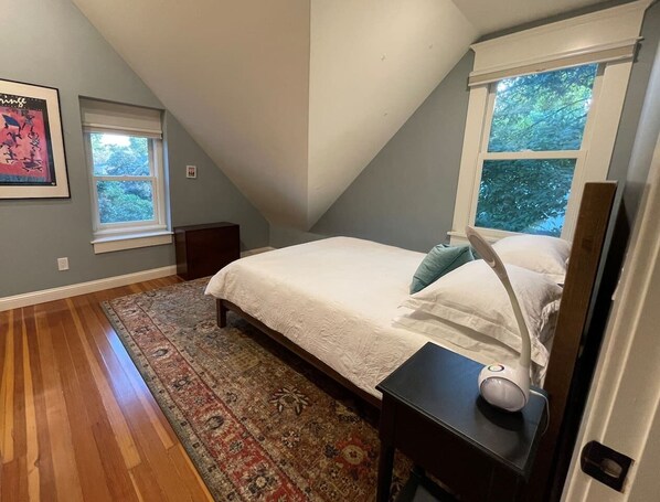 A bedroom with a bed, a nightstand, a lamp, a window, and a rug.