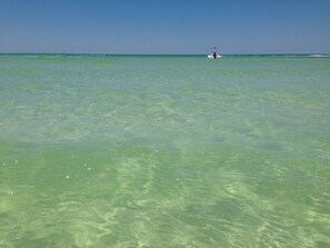 A clear view of a beach with calm waters and a distant boat.