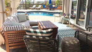 A covered outdoor area with a pool, lounge chairs, and a seating area with cushions and wicker furniture.