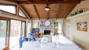 A spacious living room with a stone fireplace, a ceiling fan, and a television on a wooden stand.