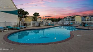 A swimming pool with lounge chairs, a white fence, and string lights against a sunset sky. - Blue Beach House, GAME ROOM, Sleep 8, Swim Pool, Gated, Casinos (Gulfport)