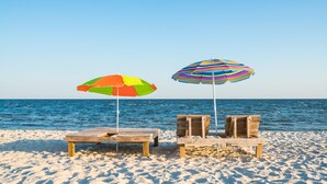 Two wooden beach chairs with colorful striped umbrellas on a sandy beach. - Blue Beach House, GAME ROOM, Sleep 8, Swim Pool, Gated, Casinos (Gulfport)