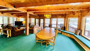 A wooden cabin interior with a dining table, chairs, a sofa, and a TV.