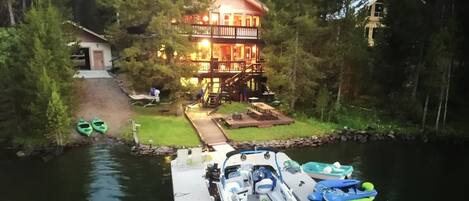 A lakeside cabin with a dock, kayaks, and a small boat.