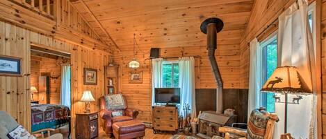 A cozy cabin interior with a fireplace, wooden walls, a television, and a comfortable seating area.