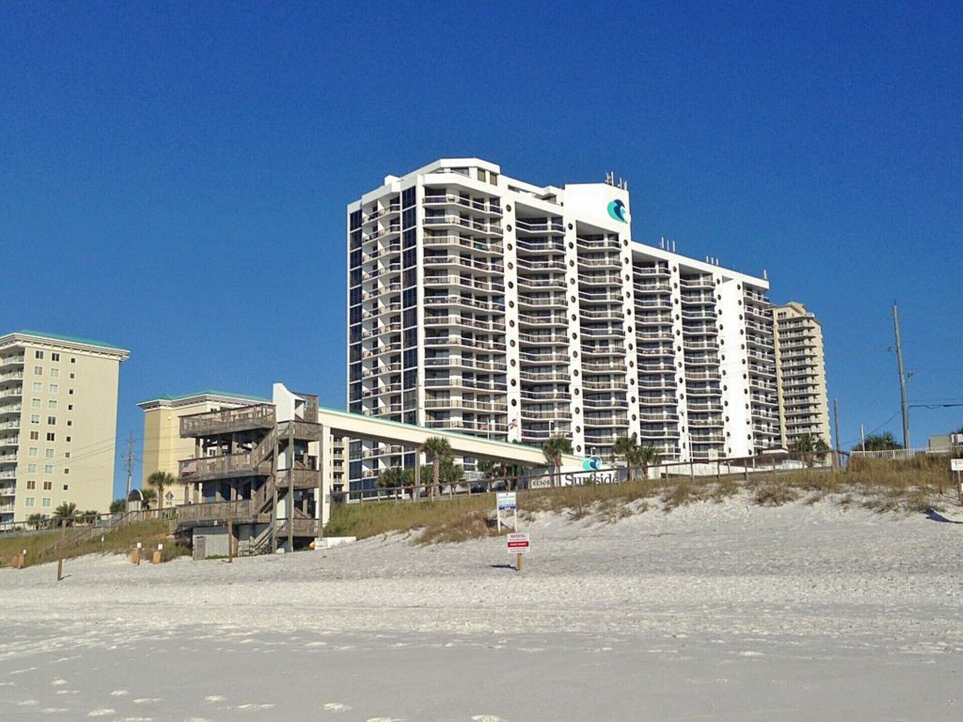 A large, multi-story hotel with a prominent 'SunSide' sign, located near a beach with a sandy foreground and a clear blue sky.