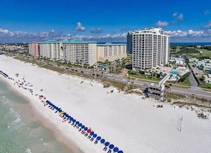 A coastal hotel with multiple high-rise buildings, a beach with umbrellas, and a road running parallel to the shore. - LAST MINUTE BOOKING SAVE 20% ! OCEAN VIEWS 2 SETS OF BEACH CHAIRS & UMBRELLAS, (Miramar Beach)